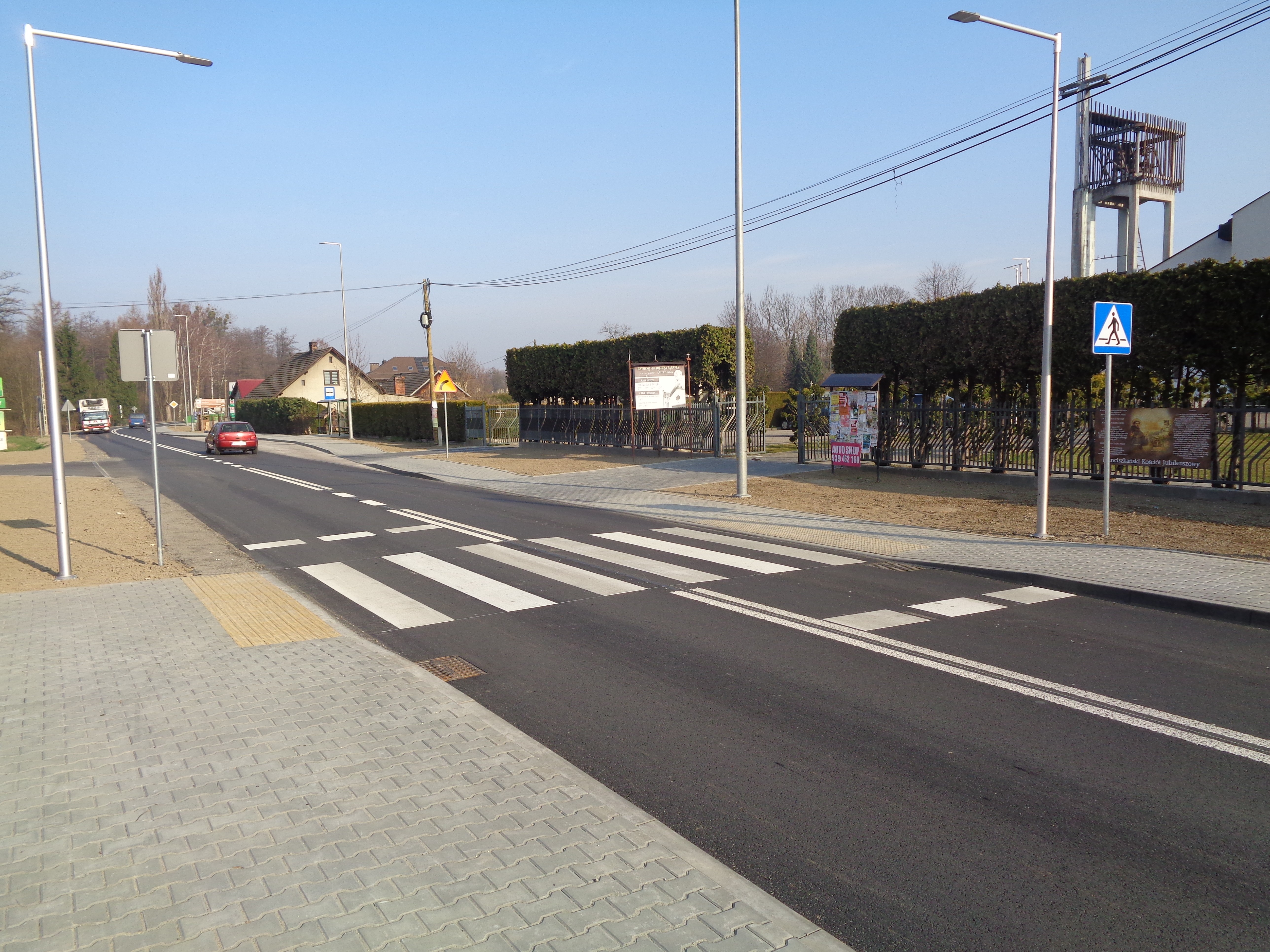 Przejście dla pieszych na jezdni, chodnik z kostki brukowej oraz znaki drogowe przy ulicy.