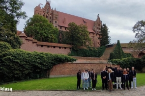  Na zdjęciu widoczna jest grupa uczniów stojących przed murami Zamku w Malborku, jednego z największych średniowiecznych zamków w Europie. Otoczenie zamku pełne jest zieleni, a w tle widać potężne gotyckie budowle, które stanowią część tego imponującego kompleksu. Zdjęcie zostało zrobione podczas wycieczki edukacyjnej w ramach programu "Podróże z klasą", której celem było poznanie ważnych historycznie miejsc w Polsce.