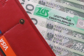 Zdjęcie przedstawia czerwoną skórzaną portmonetkę, z której wystają polskie banknoty o nominale 100 złotych, karta płatnicza Visa oraz zielona legitymacja emeryta-rencisty ZUS.