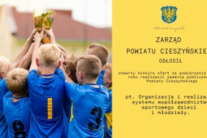 Na zdjęciu grupa dzieci w niebieskich sportowych koszulkach z numerami, trzymających wspólnie złoty puchar w geście zwycięstwa. Po prawej stronie żółte tło z herbem, napisem „Powiat Cieszyński” oraz informacją o otwartym konkursie ofert na realizację zadania publicznego w 2025 roku.