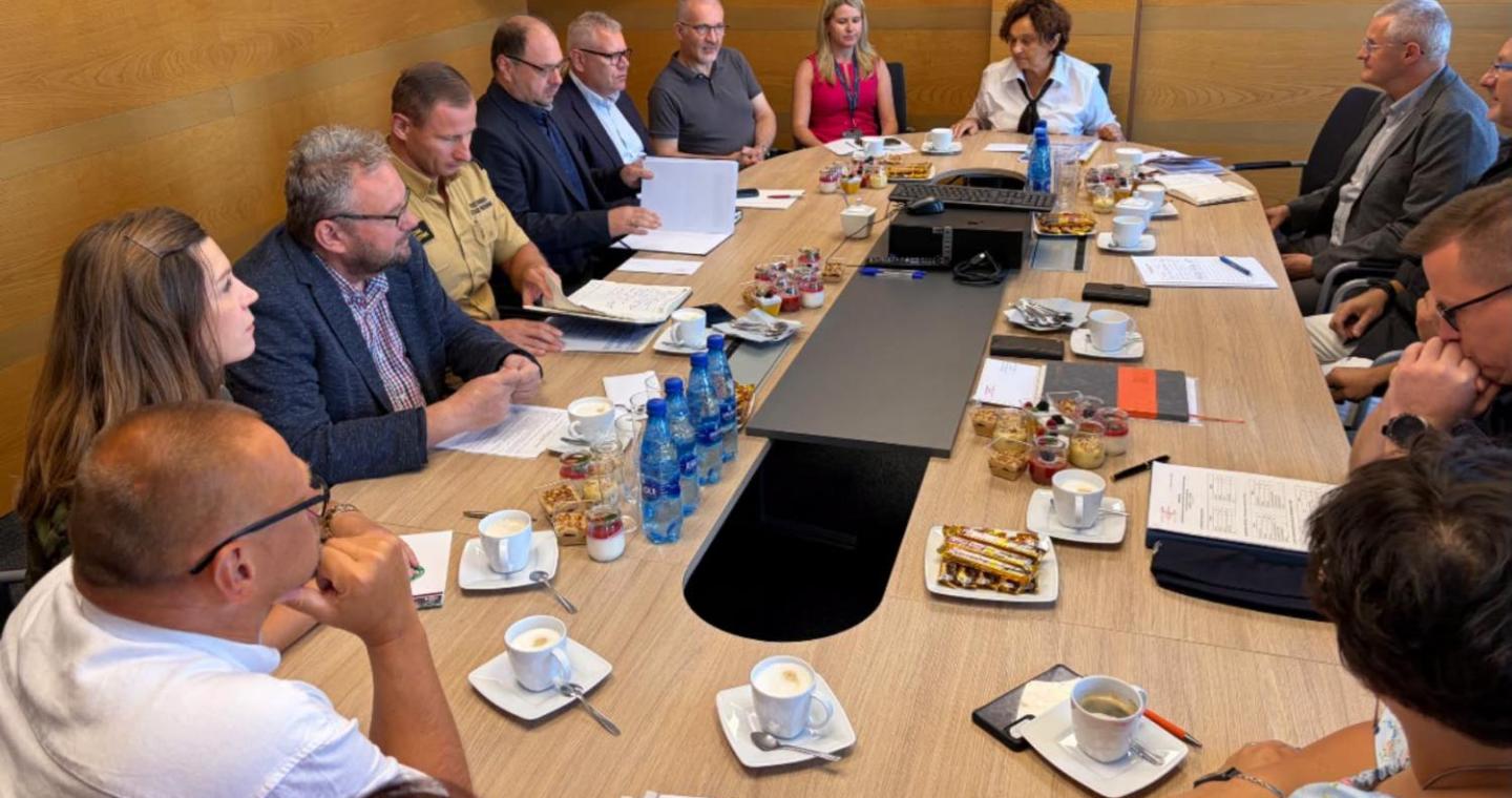 arada poświęcona bezpieczeństwu w Powiecie Cieszyńskim. Przy dużym stole konferencyjnym siedzą przedstawiciele służb, inspekcji, straży oraz samorządu. Uczestnicy mają przed sobą dokumenty i notatki, trwa rozmowa i wymiana informacji.