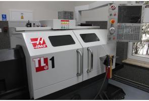 Tokarka CNC marki Haas model TL-1 w nowoczesnej pracowni; widoczne panele sterujące i okno z widokiem na drzewa.