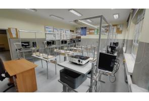 Pracownia techniczna z metalowymi stanowiskami roboczymi; na stołach monitory, sprzęt komputerowy i projektor, po lewej biurko nauczyciela - sala ZSTiO w Skoczowie.