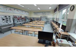 Sala dydaktyczna z komputerami ustawionymi przy oknach; w centralnej części rzędy ławek, na ścianach tablice dydaktyczne z układami elektrycznymi - sala ZSTiO w Skoczowie.