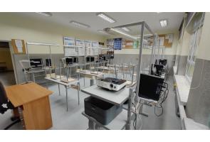Sala komputerowa z kilkunastoma stanowiskami wyposażonymi w monitory, klawiatury i sprzęt elektroniczny, ustawionymi w rzędach. Na pierwszym planie biurko z rzutnikiem w Zespole Szkół Technicznych i Ogólnokształcących w Skoczowie.