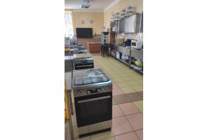 Sala gastronomiczna z kuchenkami i piekarnikami w rzędzie. Po prawej stronie blat roboczy z kuchennym wyposażeniem i szafkami wiszącymi w Zespole Placówek-Szkolno-Wychowawczo-Rewalidacyjnych w Cieszynie.