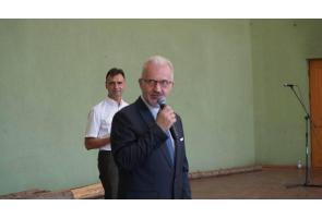 Mieczysław Szczurek Wicestarosta Cieszyński przemawia do mikrofonu, a za nim stoi mężczyzna w koszuli. Na podłodze przy ścianie znajdują się pnie drzew a z tyłu widać mikrofon na stojaku.
