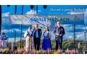Scena podczas dożynek w gminie Hażlach. Na scenie stoją cztw=ery osoby w regionalnych strojach.