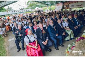 Publiczność dożynek w gminie Strumień. Ludzie siedzą ubrani w regionalne stroje w ławkach. 
