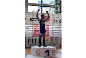Szymon Machej stoi na pierwszym miejscu podium podczas zawodów Olimpiad Specjalnych, unosi ręce w geście zwycięstwa i ma na szyi zdobyte medale.