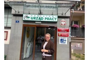 Kobieta przed Powiatowym Urzędem Pracy w Cieszynie; obok znak dostępnego wejścia dla osób na wózkach, znajdującego się z tyłu budynku.