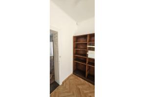 Wnętrze Domku Ogrodnika z drewnianym parkietem, białymi ścianami i dużym drewnianym regałem.