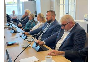 Uczestnicy sesji Rady Powiatu Cieszyńskiego siedzą przy stole konferencyjnym z tabletami i mikrofonami.
