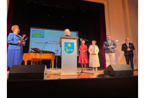 Jubileuszowa inauguracja roku akademickiego UTW w Ustroniu: kobieta przemawia przy mównicy, a obok stoją uczestnicy uroczystości; jedna z kobiet trzyma kwiaty.