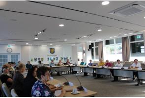 Uczestnicy VIII sesji Rady Seniorów Powiatu Cieszyńskiego siedzą przy stołach ustawionych w podkowę; za nimi widnieje herb powiatu.