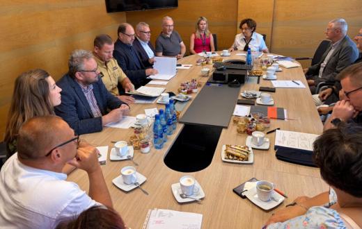 arada poświęcona bezpieczeństwu w Powiecie Cieszyńskim. Przy dużym stole konferencyjnym siedzą przedstawiciele służb, inspekcji, straży oraz samorządu. Uczestnicy mają przed sobą dokumenty i notatki, trwa rozmowa i wymiana informacji.