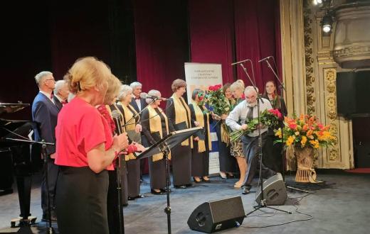 Uroczysta inauguracja Uniwersytetu Trzeciego Wieku w Cieszynie: uczestnicy stoją na scenie, a mężczyzna wręcza kobiecie bukiet kwiatów.